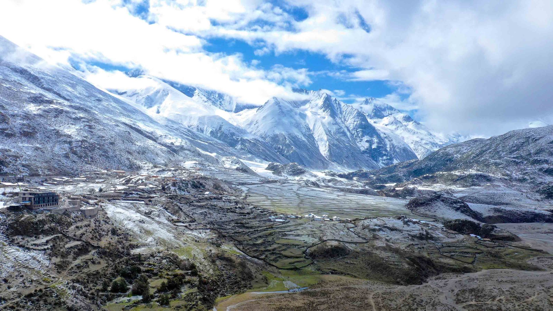 Snow-dusted Rawu valley beneath glaciated peaks, with Songtsam Lodge Laigu on the hillside