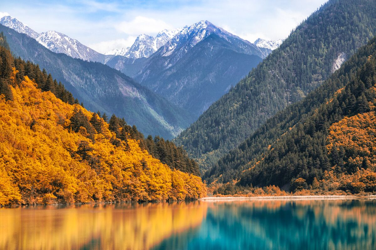 Turquoise lake fringed by autumn forest and snow-capped peaks in Jiuzhaigou