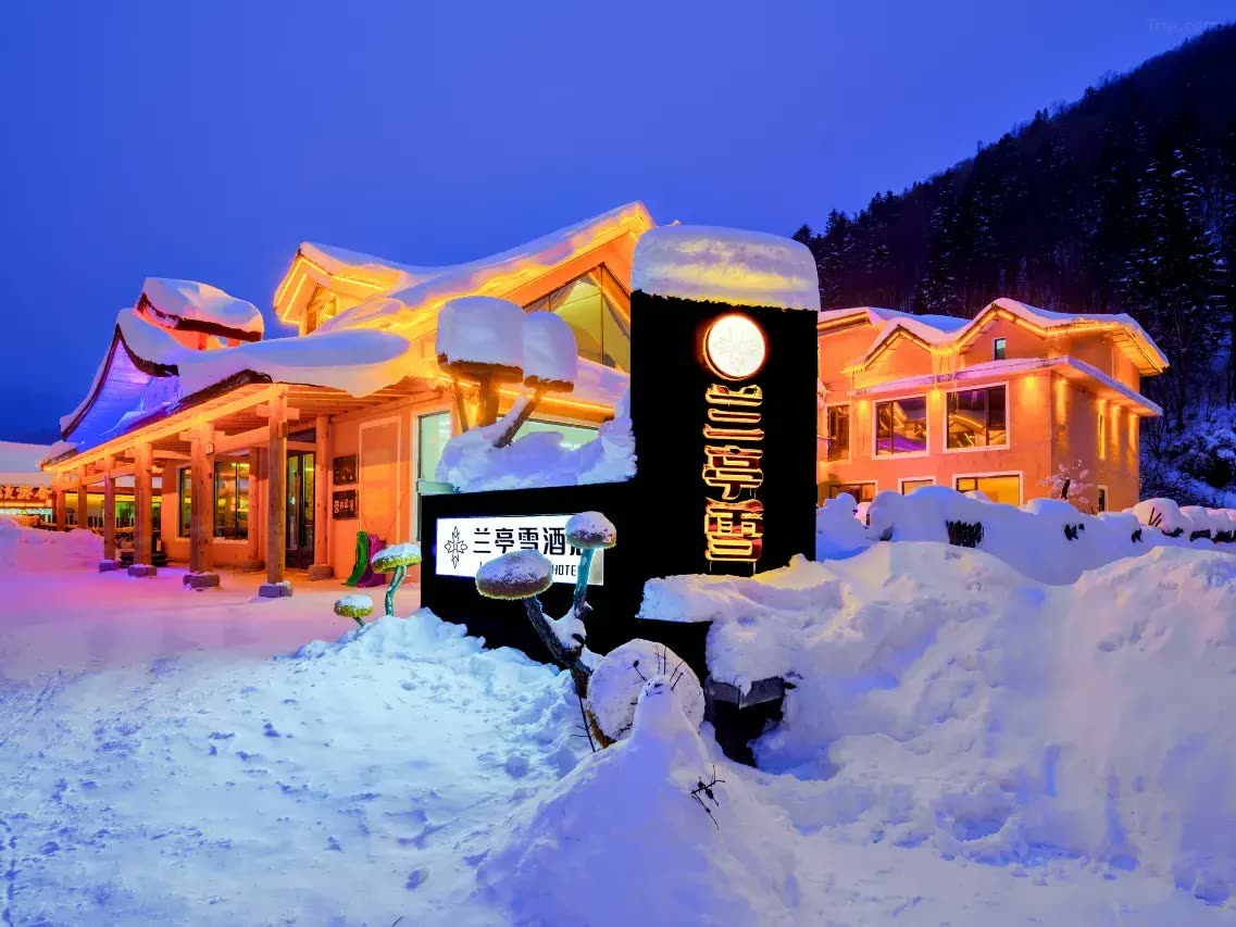 Lanting Snow Hotel lit at dusk under deep snow, China Snow Town